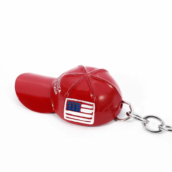 Red hat-shaped keychain with "Make America Great Again" text and USA flag lying flat on white background.