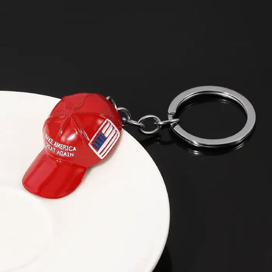 Red hat keychain featuring "Make America Great Again" text and USA flag placed on a white ceramic dish.