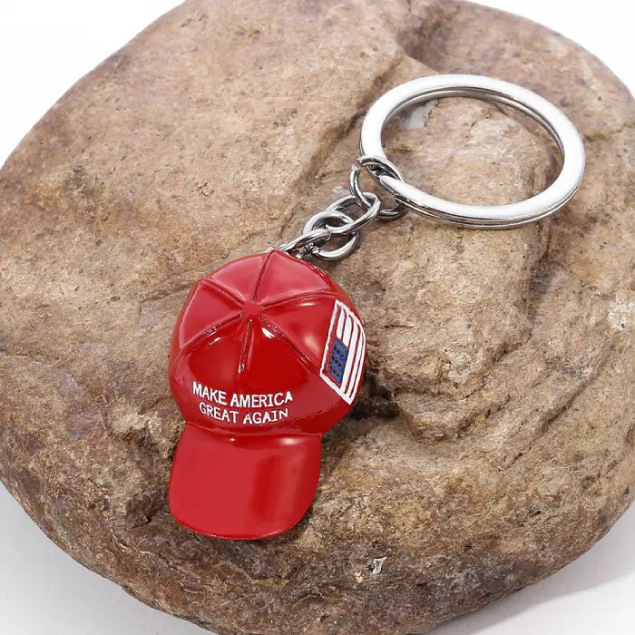 Red hat keychain with "Make America Great Again" text and USA flag placed on a textured rock.