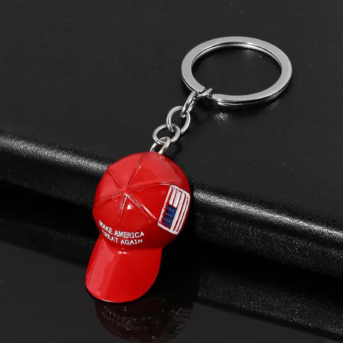 Side view of red hat keychain featuring "Make America Great Again" text and USA flag on black surface.