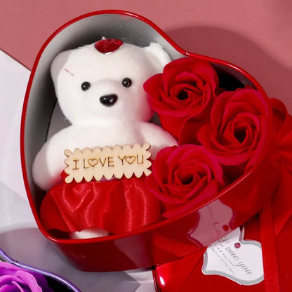 Closeup of red heart box with plush teddy bear holding love message and red roses