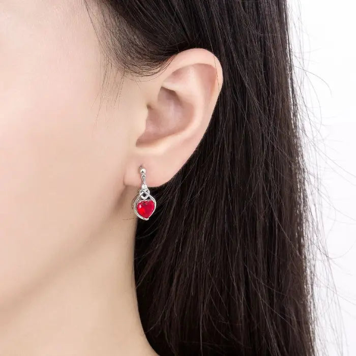 Close-up of a silver earring with a heart-shaped red gemstone worn on an ear for a classy look.