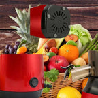 Slow masticating juicer with red base next to wicker basket filled with fresh fruits on wooden background