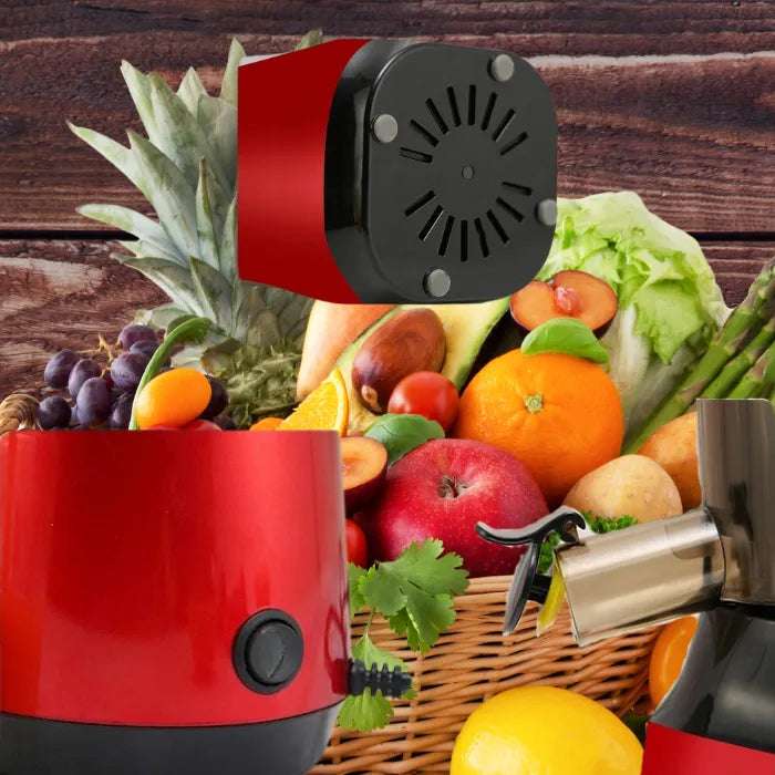 Slow masticating juicer with red base next to wicker basket filled with fresh fruits on wooden background