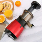 Red slow juicer on marble countertop with fresh orange juice and breakfast setting demonstration