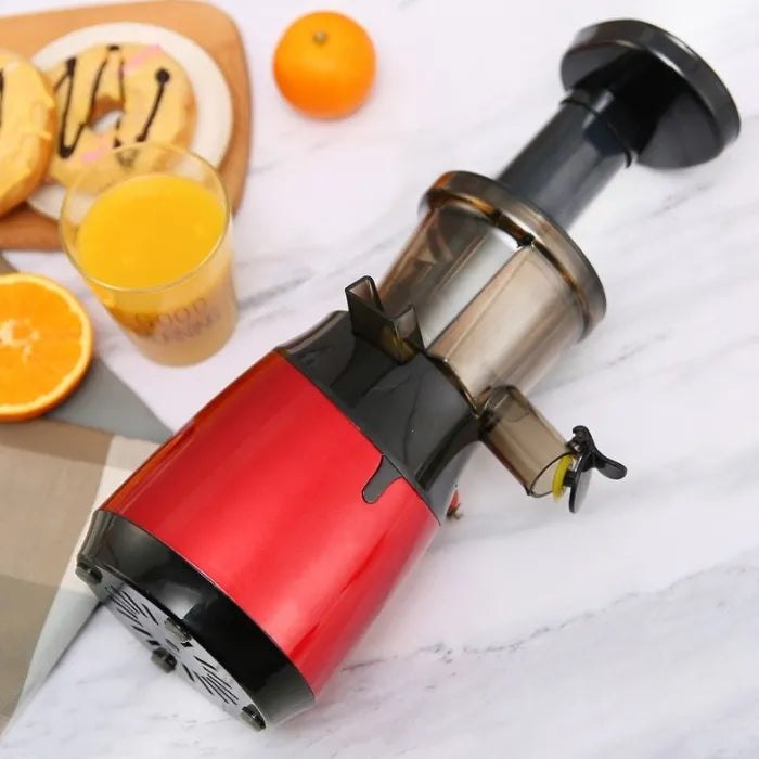 Red slow juicer on marble countertop with fresh orange juice and breakfast setting demonstration