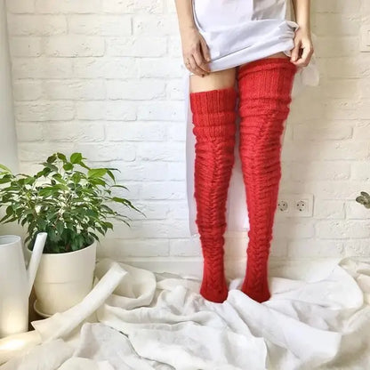 Person wearing long red knit socks, white shirt, against white brick wall with potted plant and fabric