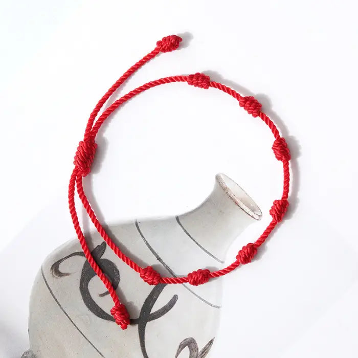 Decorative red seven-knot bracelet with a secure adjustable string for luck and protection.