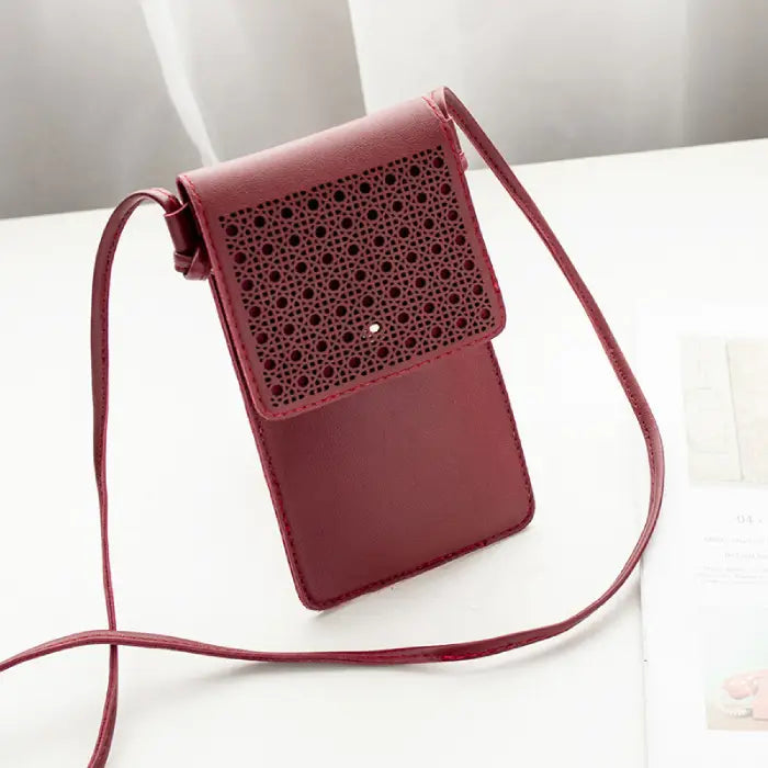 Red leather crossbody phone bag with a decorative perforated flap, displayed on a white surface.