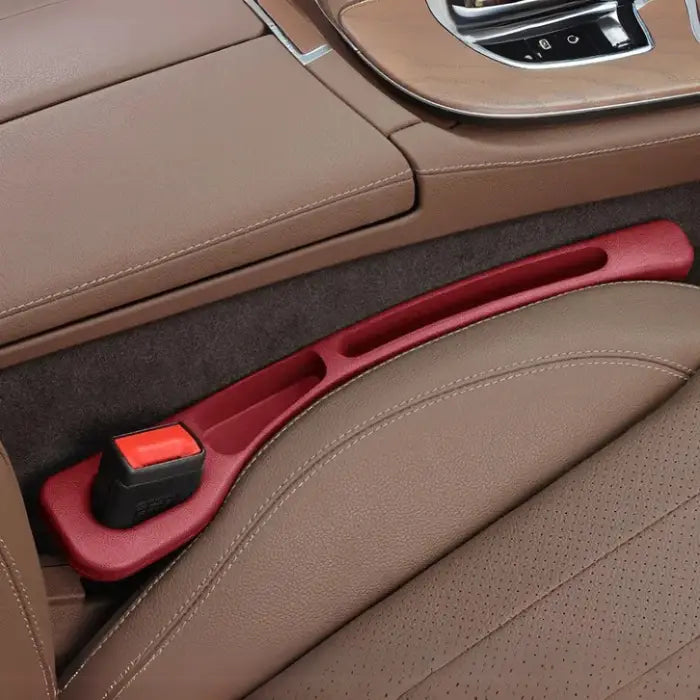 Red car seat gap filler installed in luxury vehicle with brown leather upholstery