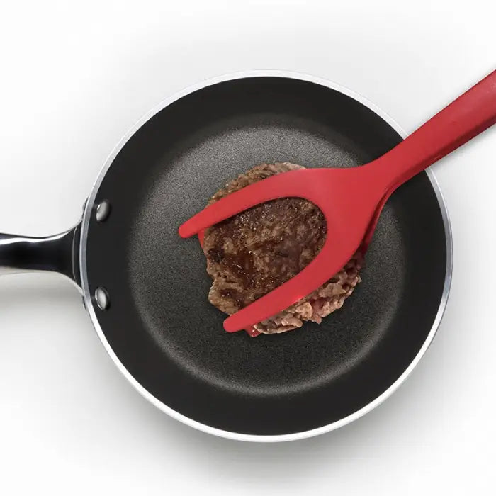 Red silicone spatula flipping a beef patty in a non-stick frying pan for easy cooking.