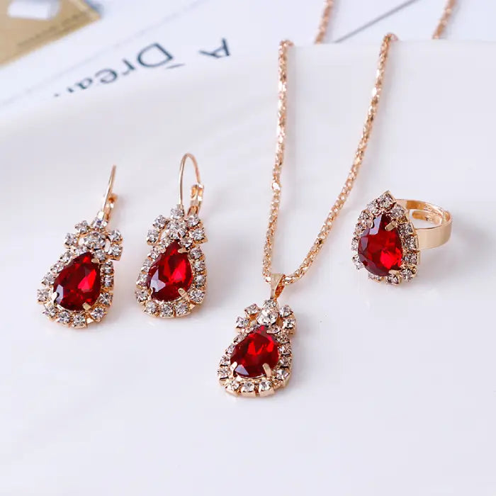 Red teardrop gemstone jewelry set including necklace, earrings, and ring with gold and crystal accents.