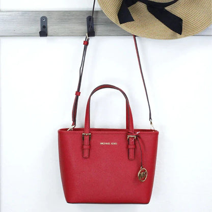 Luxury red leather Michael Kors jet set tote with gold charm displayed on gray wall hook next to decorative straw hat