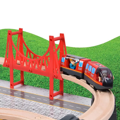 Red toy train crossing a wooden bridge on a railway track surrounded by greenery.