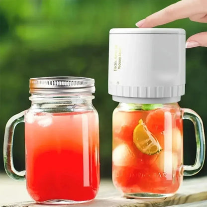 Hand placing white electric vacuum sealer on mason jar filled with colorful fruit drink next to another jar with red beverage