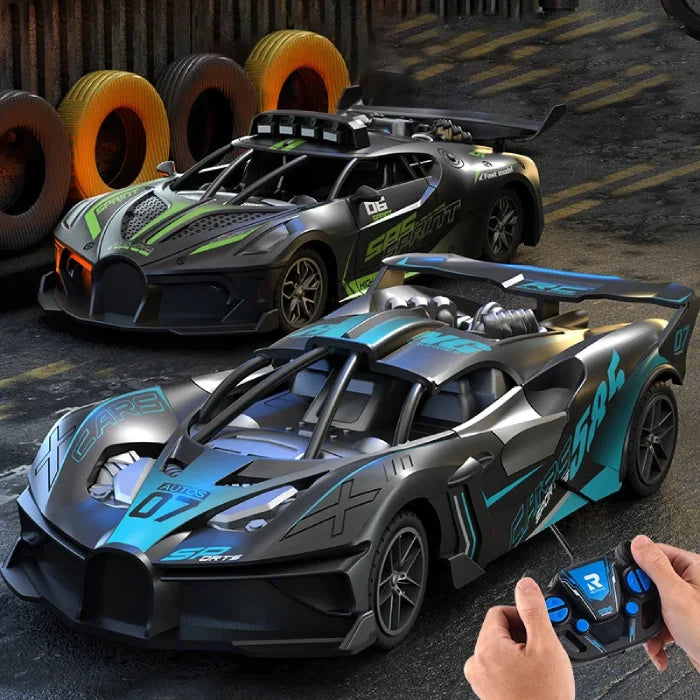 Green and blue remote control racing cars near stacked tires on a race-themed track, with a user holding a controller.