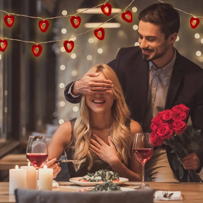 Romantic dinner scene with couple and red heart lights, perfect for Valentine's.