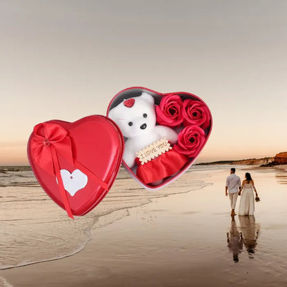 Red heart gift box with teddy bear and roses against romantic beach sunset with couple walking