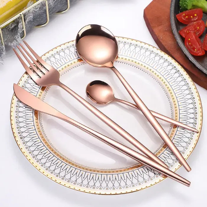 Rose gold cutlery set displayed on decorative plate with geometric pattern border, alongside food presentation