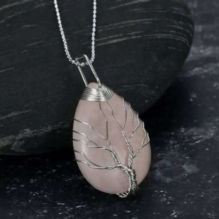 Rose quartz teardrop pendant with wire tree of life design and silver chain on dark stone background.