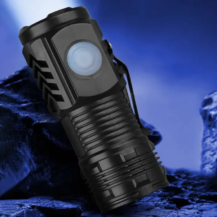 Durable black LED flashlight showcased in a rugged outdoor setting with a glowing light.