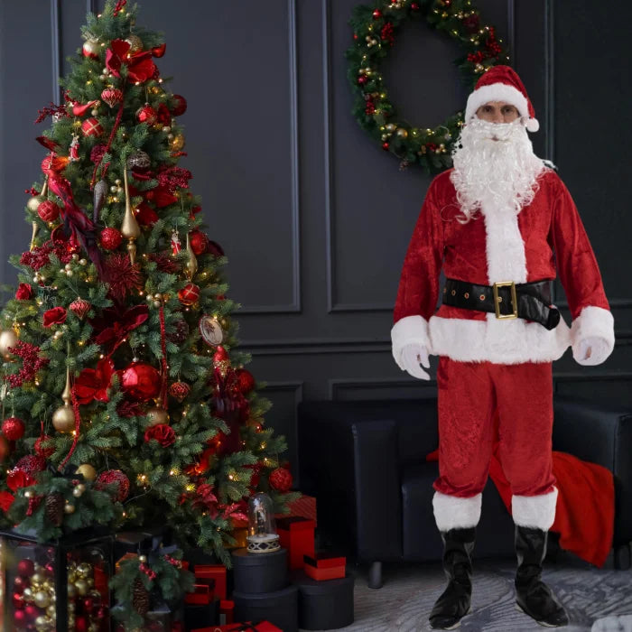 Santa costume adult posing beside Christmas tree and wreath in dark festive interior.