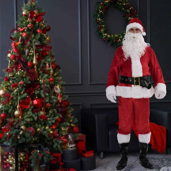Santa costume adult posing beside Christmas tree and wreath in dark festive interior.