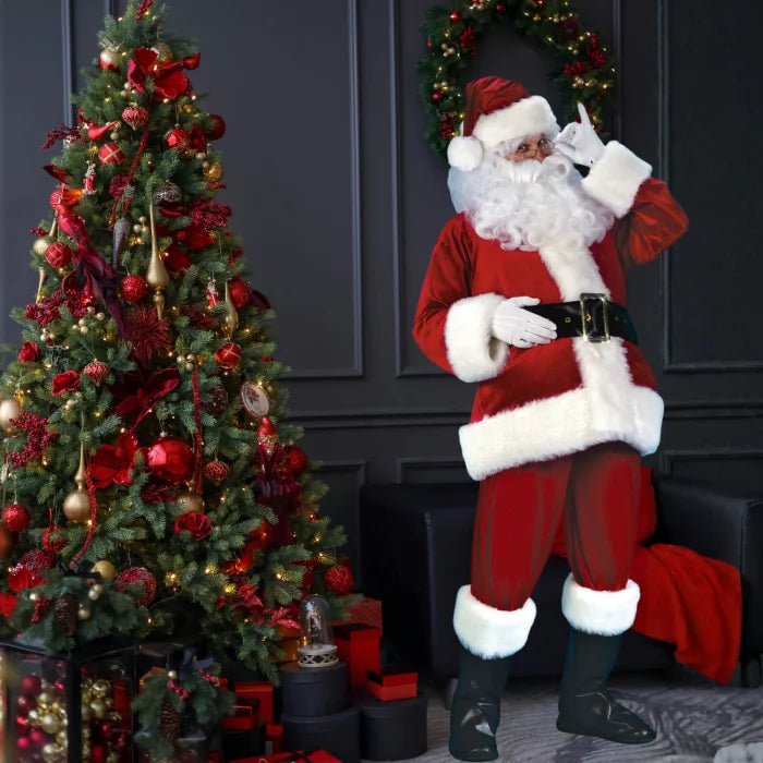 Santa costume adult standing near red and gold Christmas tree with presents and festive decor.