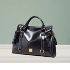 Satchel handbag in black leather with tassel details shown on display table with green wall