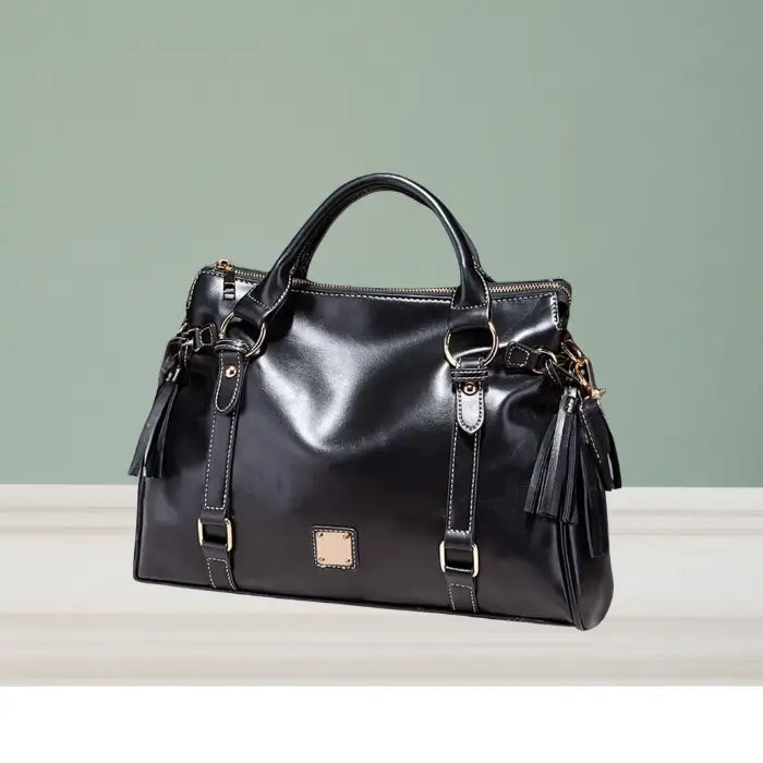 Satchel handbag in black leather with tassel details shown on display table with green wall