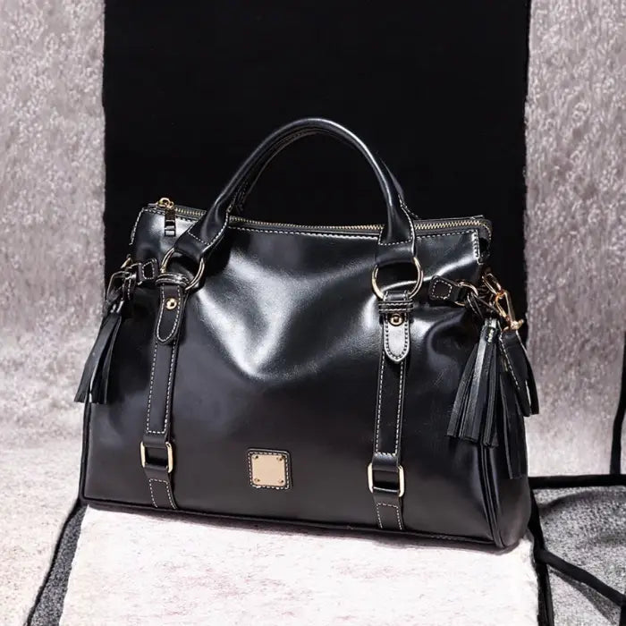 Satchel handbag in black leather on soft beige and black display background
