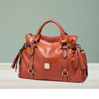 Satchel handbag in classic brown leather with tassels displayed on tabletop background