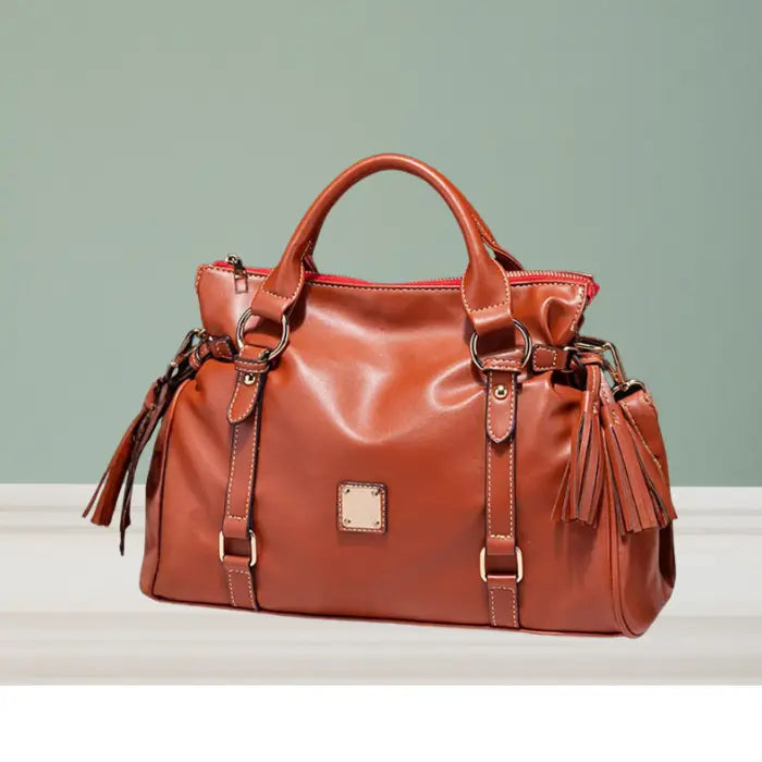 Satchel handbag in classic brown leather with tassels displayed on tabletop background