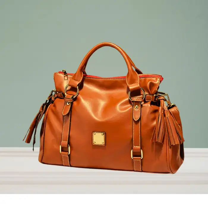Satchel handbag in caramel leather with tassels and gold hardware on clean white background
