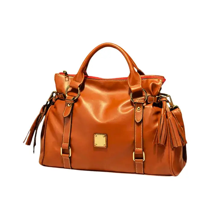 Satchel handbag in caramel leather with tassels shown on tabletop and light green background