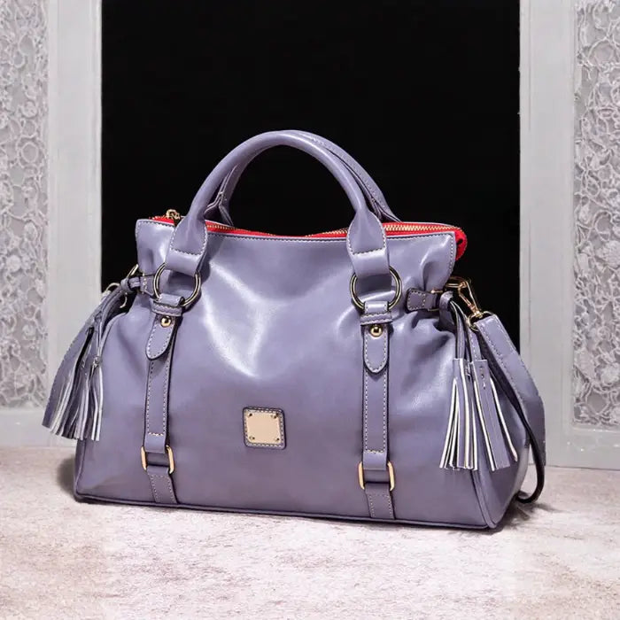 Satchel handbag in soft purple leather with tassels shown against window and black backdrop