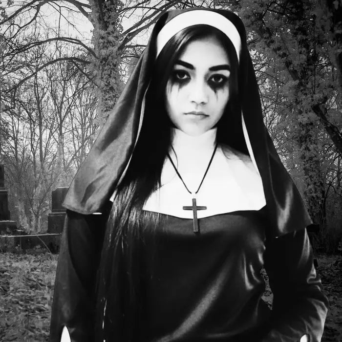 Scary nun costume in black and white photo standing in overgrown cemetery with serious expression.