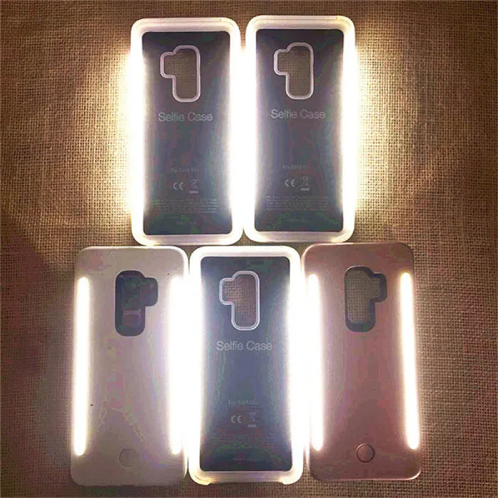 Brightly lit selfie cases with LED lights on, shown on textured background in assorted colors.