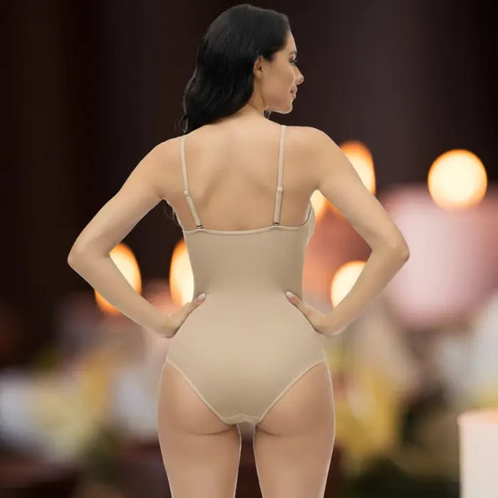Rear view of beige shapewear underwear bodysuit with model posing hands on hips in indoor light.