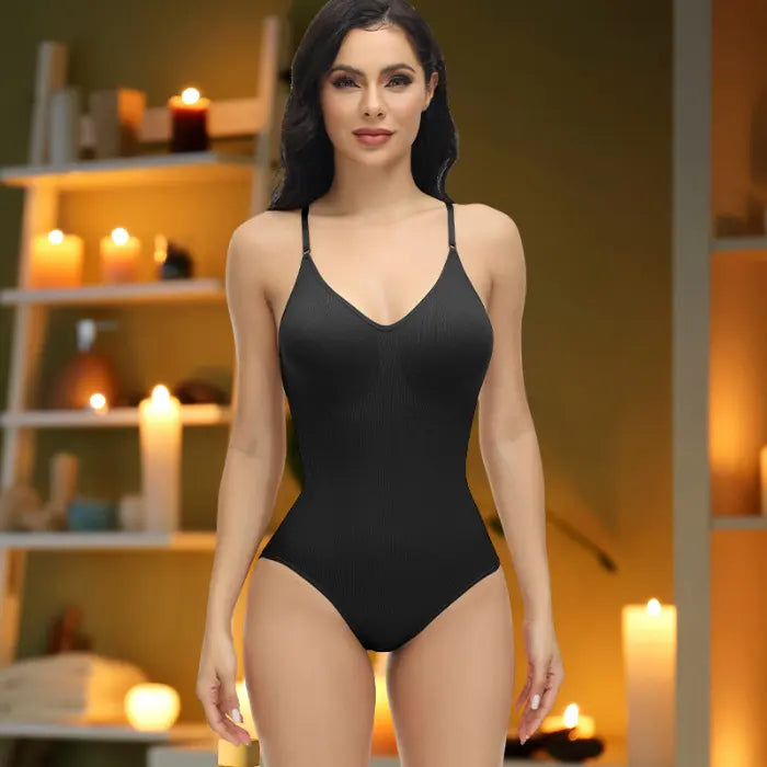 Model in black shapewear underwear bodysuit standing front-facing in spa-inspired candlelight room.