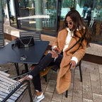 sherpa coat in tan with hoodie and ripped jeans, sitting outdoors with coffee and black purse.