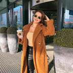 sherpa coat in brown styled with black pants, beige top, and coffee cup on a sunny city street.