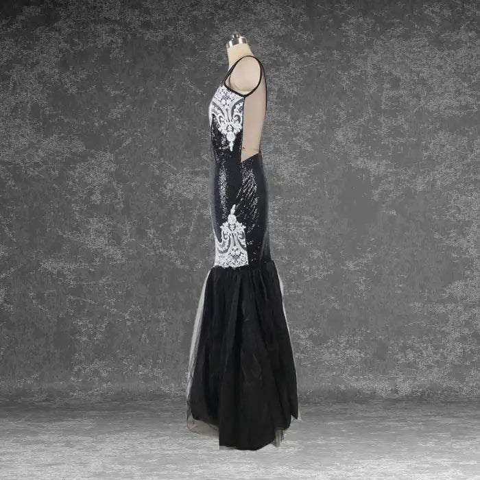 Side profile of mannequin displaying the black sequin mermaid dress silhouette with white lace appliqué and tulle skirt