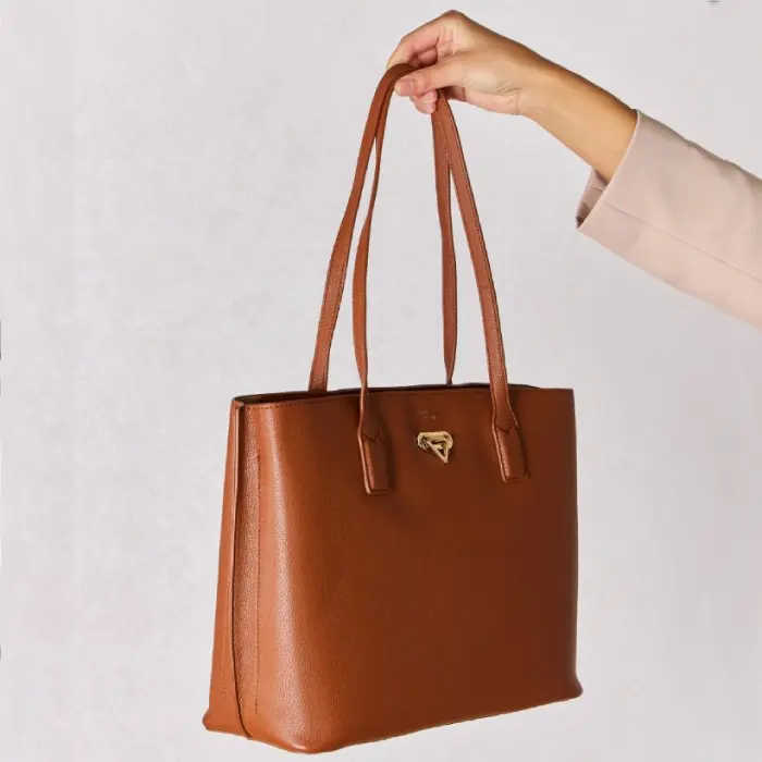 Side view of brown leather tote bag held by hand, showcasing its spacious interior and gold hardware detail