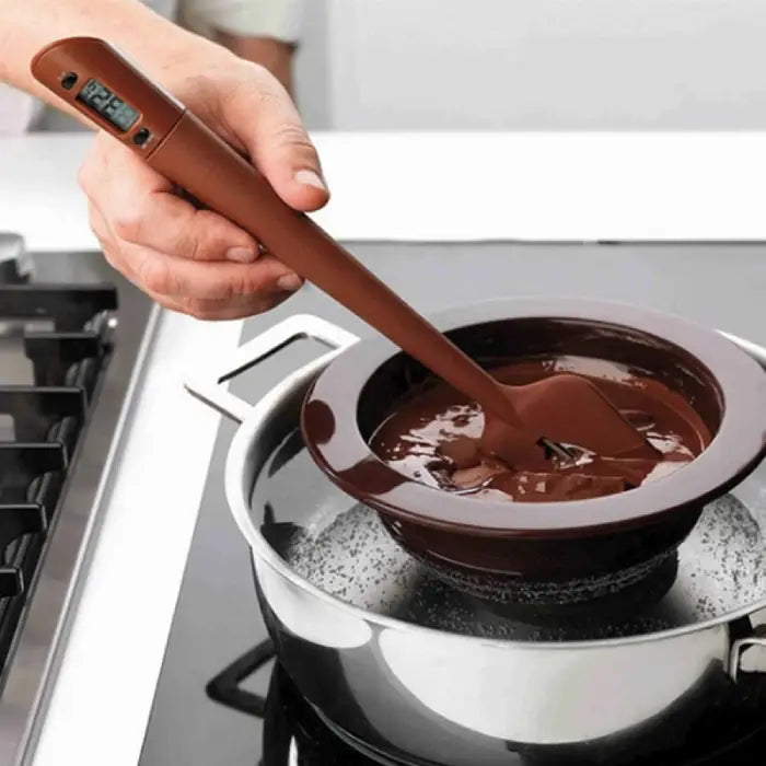 Silicone thermometer spatula in action stirring melted chocolate in double boiler with digital temperature display visible