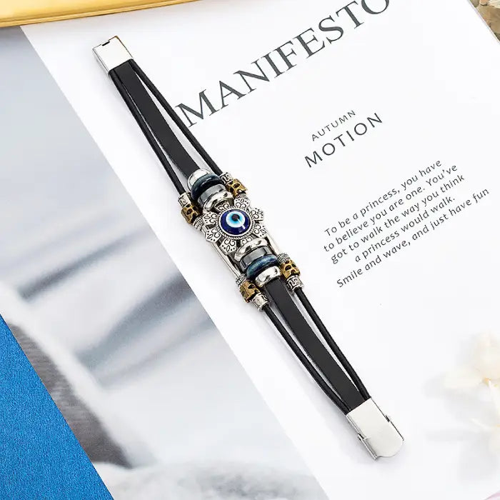 Silver and blue evil eye bracelet displayed on a manifesto-themed background with leather straps.