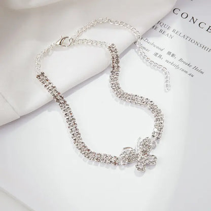 Silver butterfly chain anklet featuring sparkling crystals on a white surface with reading material backdrop.