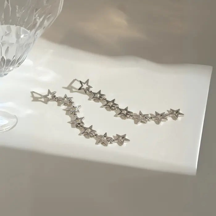 Silver star drop earrings arranged on white paper with soft shadows