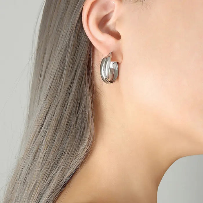 Silver-toned thick hoop earring shown on ear with grey hair and minimalist styling