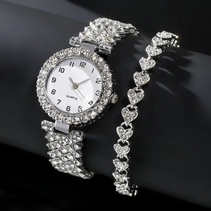 Silver diamond like-studded quartz wristwatch with a matching heart-shaped bracelet displayed on a black background.